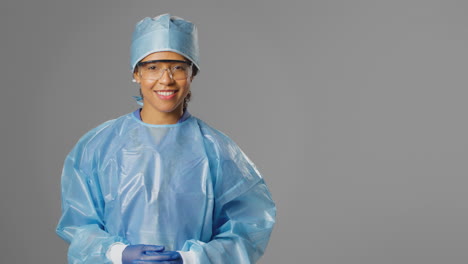 portrait of smiling female surgeon wearing safety glasses and against grey background