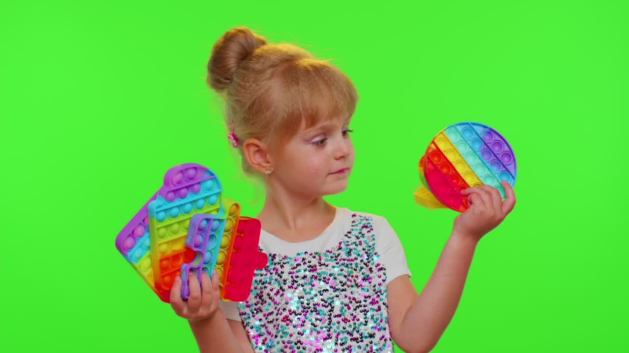 Flicka som håller och klämmer en populär antistressleksak, en 'push pop it', mot green screen.