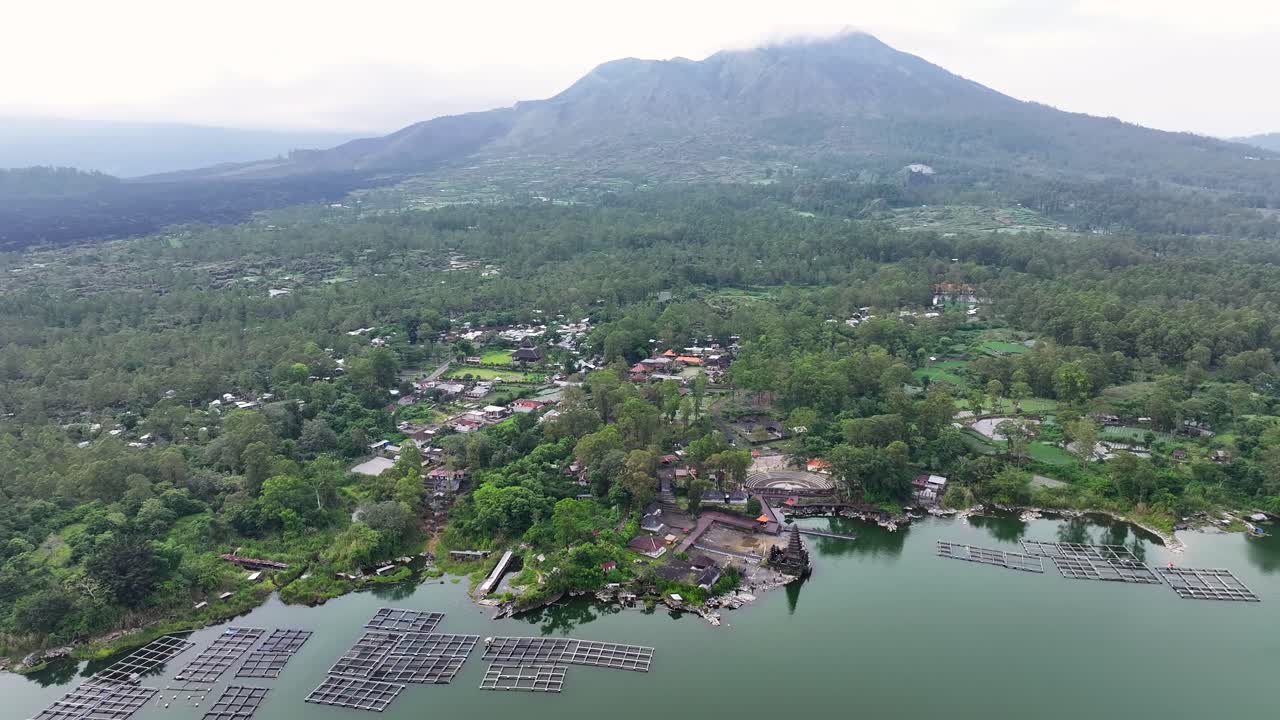 Aerial view over Pura Segara Ulun Danu Batur temple on lake and volcano on horizon, Bali.