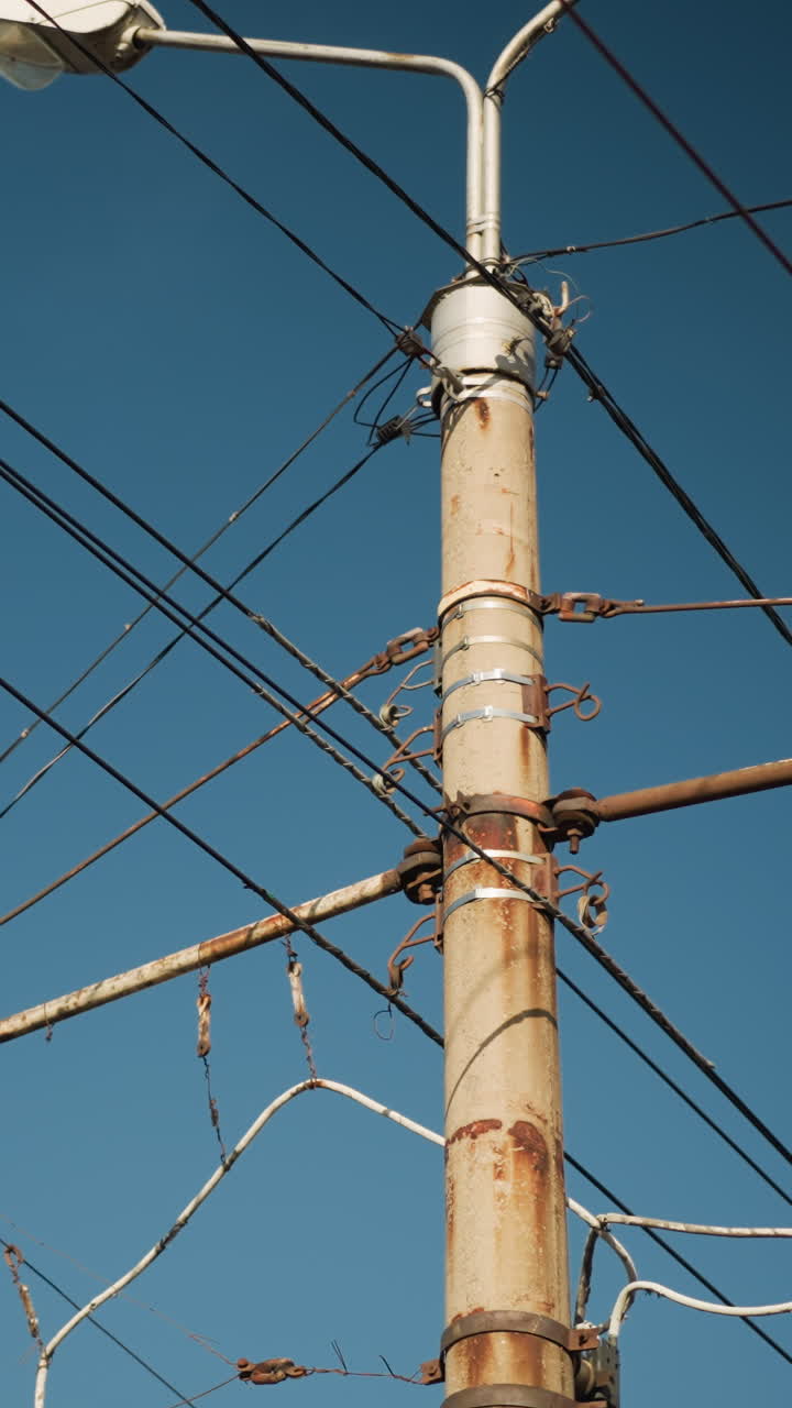 Poste de servicios oxidado sobre un cielo despejado, cables enredados y accesorios metálicos en vista vertical de primer plano, aislantes desgastados, ambiente urbano diurno, situación de mantenimiento con posible inspección de electricista