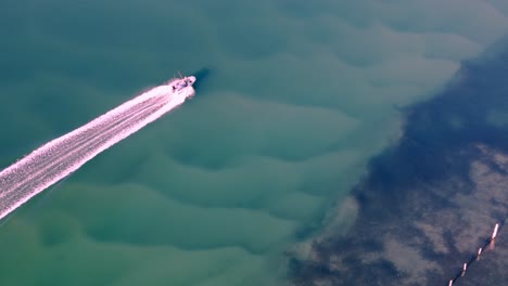 a small boat running over a body of sea water, aerial view, superflat, sand, beach