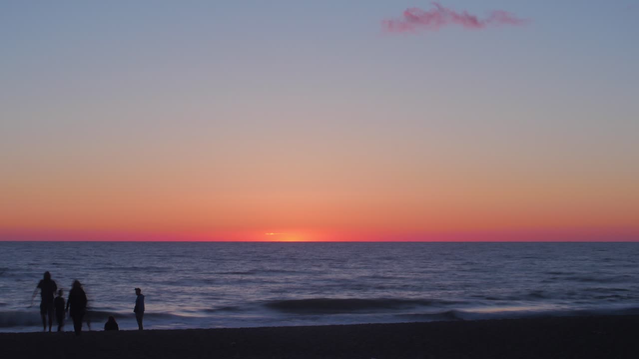Time lapse of beautiful scenic beach view at sunset with silhouettes of people at the seaside, wide shot