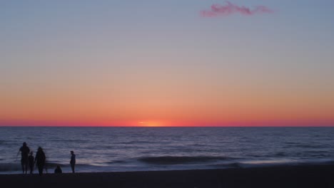 lapso de tiempo de hermosa vista panorámica de la playa al atardecer con siluetas de personas en la orilla del mar, toma amplia