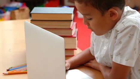 vista lateral de un escolar asiático atento estudiando con una computadora portátil en un aula de la escuela 4k