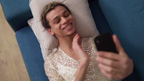 Cheerful-guy-in-fancy-dress-doing-selfie-with-mobile-phone-lying-on-sofa