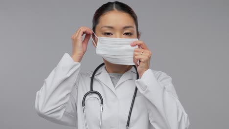 Glückliche-Asiatische-Ärztin-Zeigt-Medizinische-Maske.Medizin-,-Berufs--Und-Gesundheitskonzept-–-Videoporträt-Einer-Glücklich-Lächelnden-Asiatischen-Ärztin-Im-Weißen-Kittel-Mit-Stethoskop,-Die-Zeigt,-Wie-Man-Eine-Medizinische-Maske-Auf-Grauem-Hintergrund-Verwendet