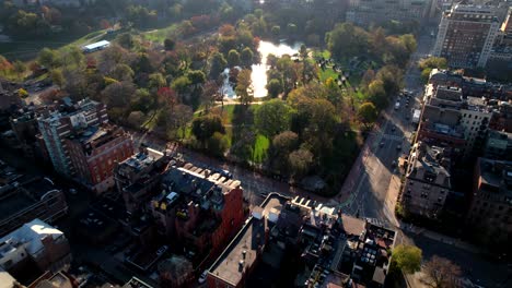 drone flyover downtown apartments towards boston common public garden, sunlight reflected on lake surface