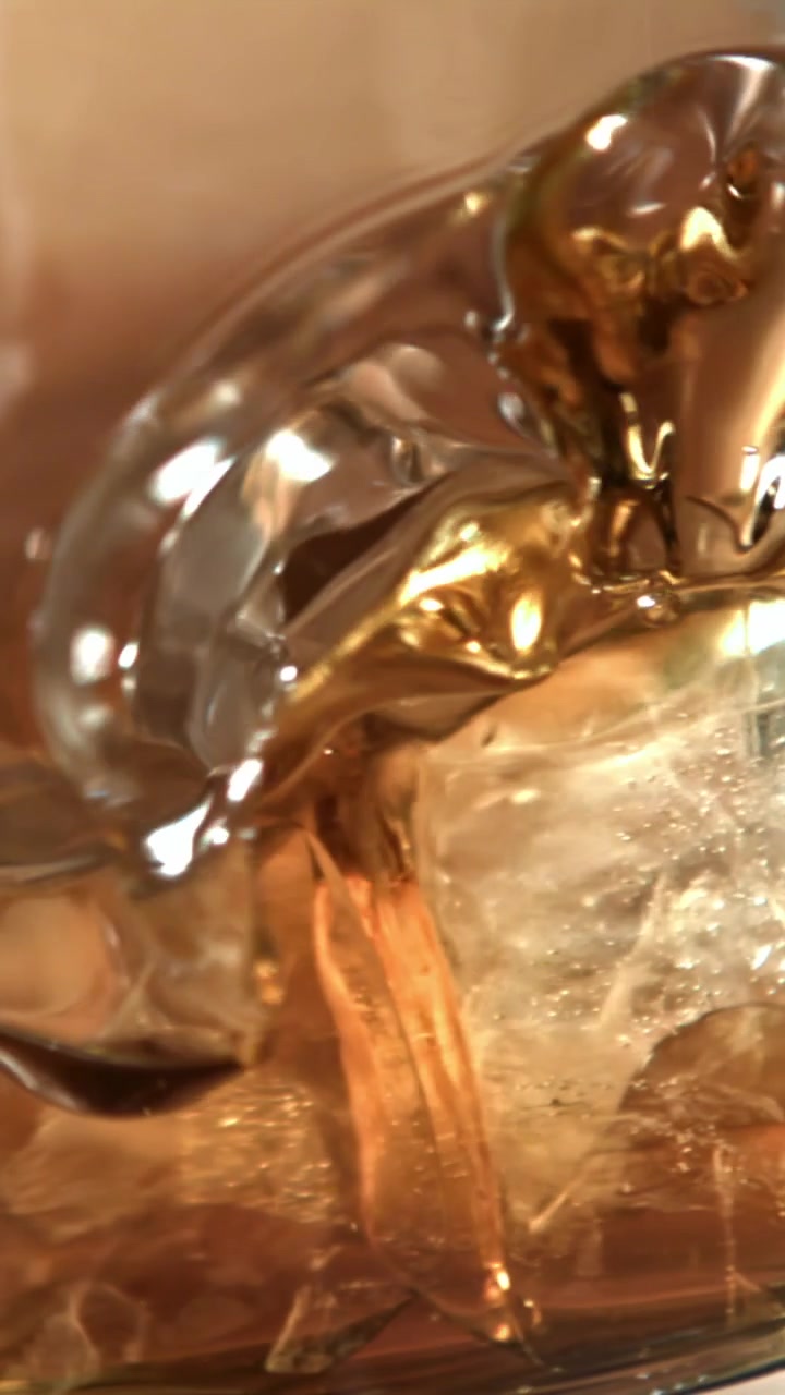 Versamento di liquido dorato su cubetti di ghiaccio in un bicchiere