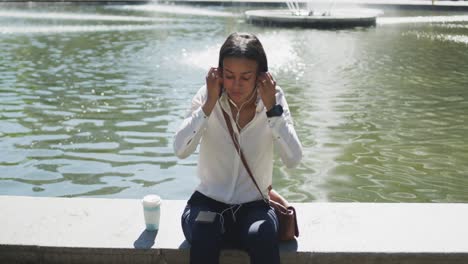 african american woman putting earphones on in city park