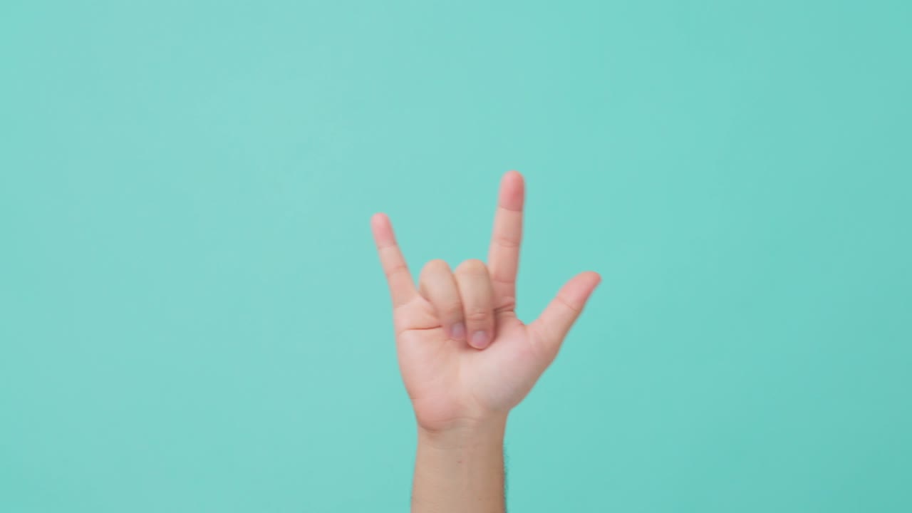 Close up shot of human hand raising, making hand gesture love-you gesture or I love you hand sign emoji by raised index finger and little finger and a thumb. Seen in isolate blue screen in background.
