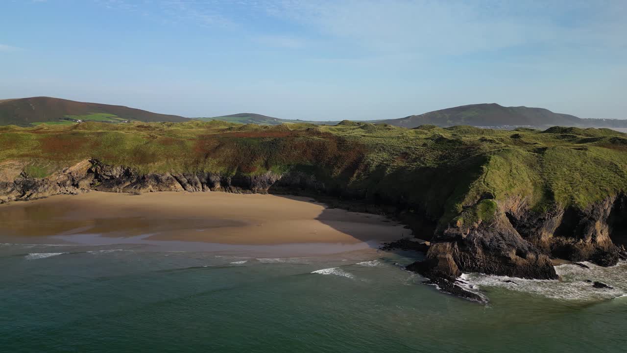 una toma aérea lateral del drone de la costa de gower con olas y acantilados en la piscina azul de broughton bay