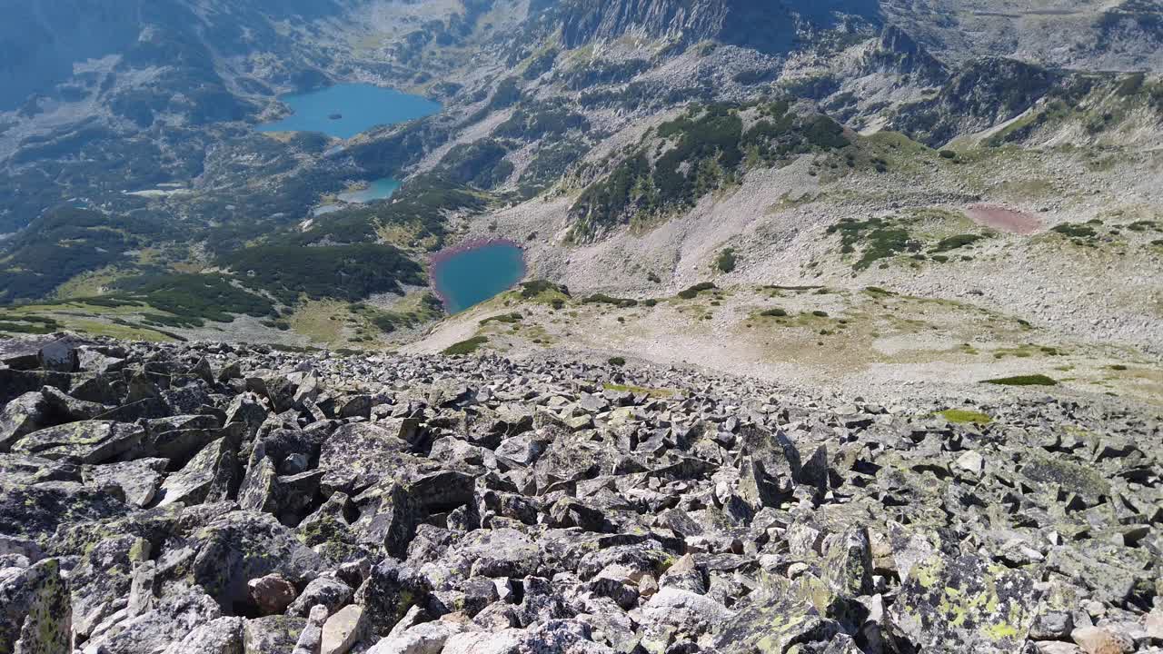 View from the top to a high and steep stone peak. Mountain lakes. Green hills. Beautiful views. Tilt up. Northern Pirin, Bulgaria.