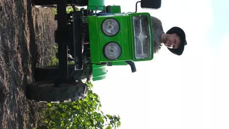 a handsome farmer is driving a tractor black and red currant bushes grow in rows on the plantation a handsome farmer drives a tractor across a field with currant bushes currant bushes in even roves on farm land growing berries agribusiness