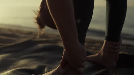 flexible sportswoman bending body to feet on beach closeup. yoga woman training