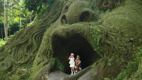 Female-Tourist-And-Daughter-Posing-At-Mouth-Cave-In-Alas-Harum-Bali,-Tegallalang,-Indonesia