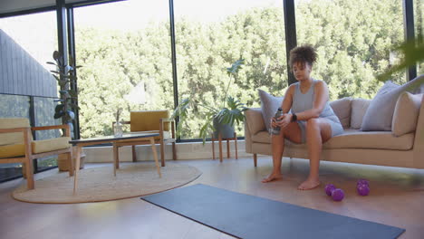 resting on sofa, plus size woman holding water bottle after home workout, copy space
