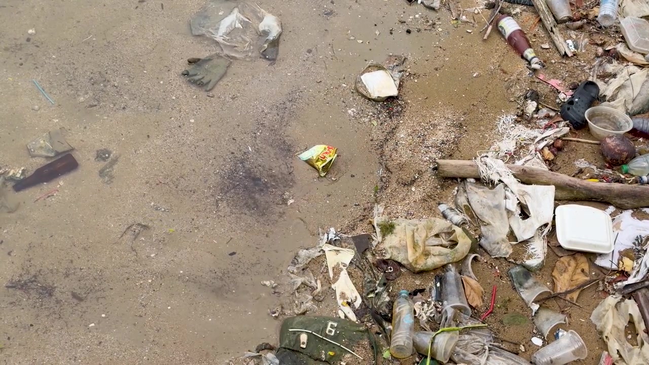 Overhead static shot of plastic debris and garbage washed up on a wet sandy shoreline.