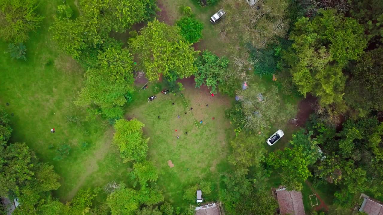 Aerial view of tourists playing volleyball in a campsite in Uganda, Africa, surrounded by lush green vegetation and trees, enjoying their vacation, top down descending drone shot