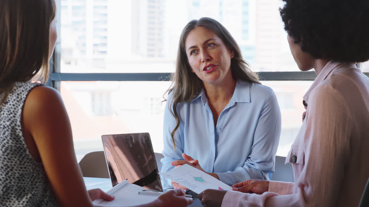 equipo de negocios multicultural femenino se reúne alrededor de la mesa de la sala de juntas con computadoras portátiles discutiendo documentos