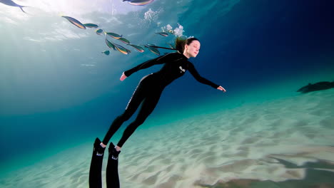 freediver swimming with a school of fish in clear tropical waters