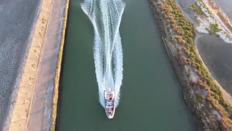 vista vertical aérea de un avión no tripulado siguiendo un barco rápido en un canal durante la puesta del sol.