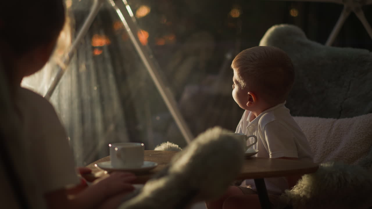 아이들은 텐트에서 테이블에 앉아, 형제자매들은 차를 마시며, 호텔의 빛이 비치는 창문 밖을 쳐다보며 느린 동작으로, 차분한 아이들은 아침에 글램핑 텐트에서 휴식을 취합니다.