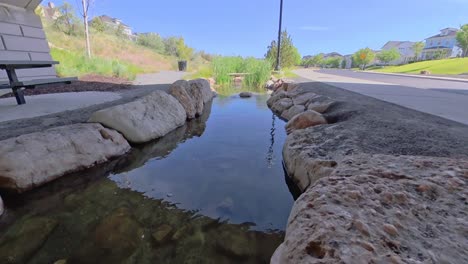 camera glides over shallow stream running under bridge beside suburban road