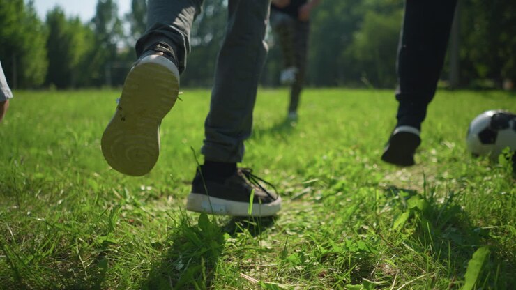 Close up leg view of people jumping on a grassy field, with a blurred goal post in the background