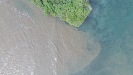 Top-down-aerial-drone-shot-over-polluted-sewage-water-and-floating-trash-with-debris-over-dead-coral-reef-mixing-with-turquoise-water-and-tropical-coastine-in-Bali-Indonesia