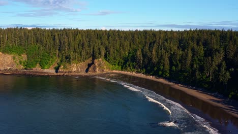 impresionante carro de drones aéreos en una toma de la hermosa tercera playa en forks, washington con un bosque o grandes pinos verdes en los acantilados en una cálida y soleada mañana de verano con nubes.