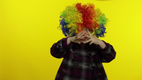 una niña payasa con una peluca arco iris haciendo caras tontas. divirtiéndose, sonriendo, bailando. halloween
