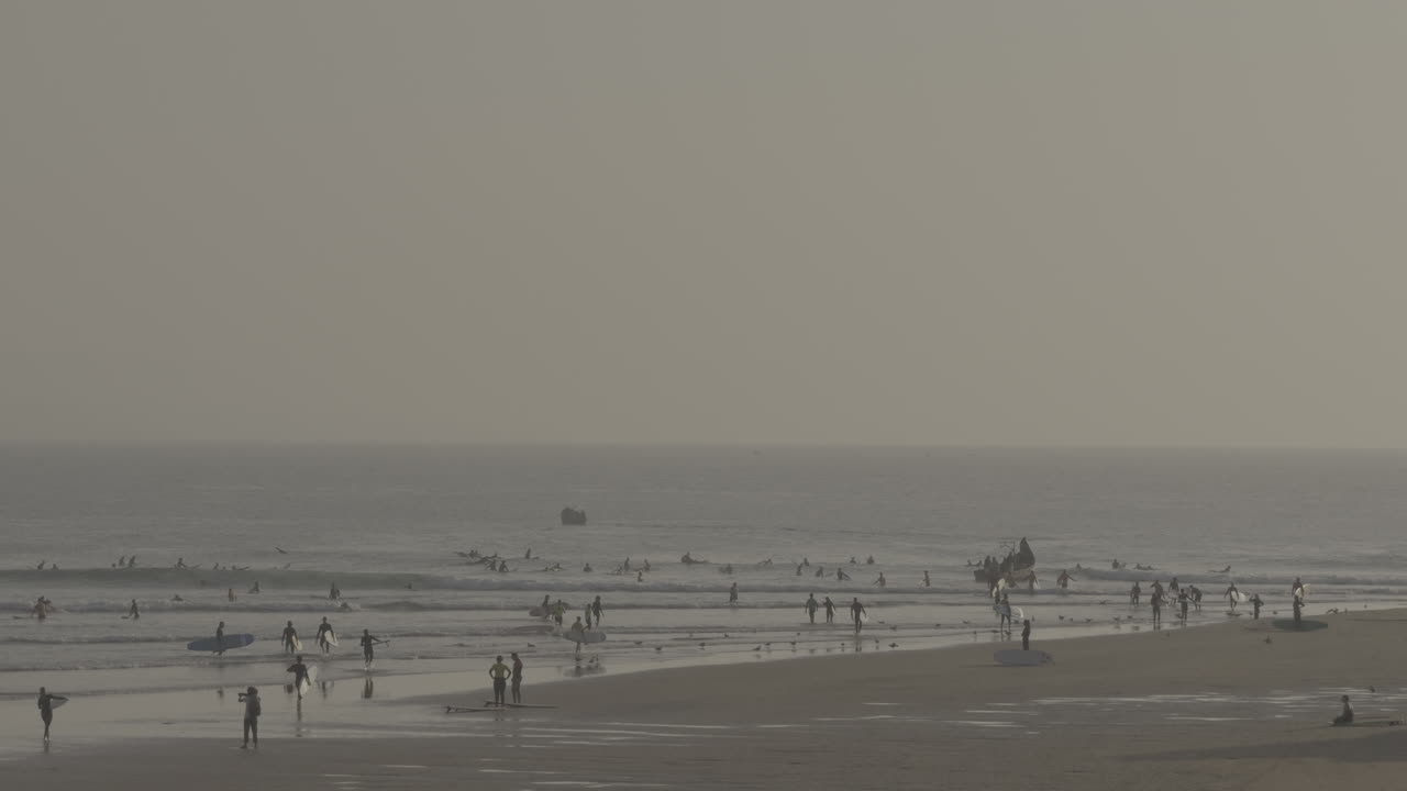 Surfers at a beach with a hazy sky