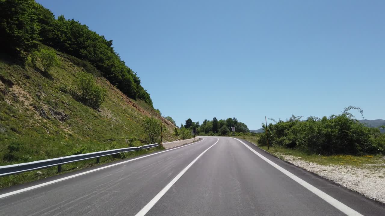 Pohled z jedoucího vozidla (auto, motorka nebo jízdní kolo) na horskou krajinu