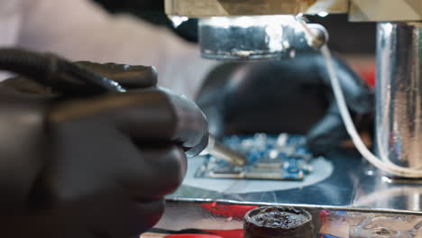 a close-up view of a technician's hand holding a soldering iron with smoke rising, indicating the soldering process, with other tools in view