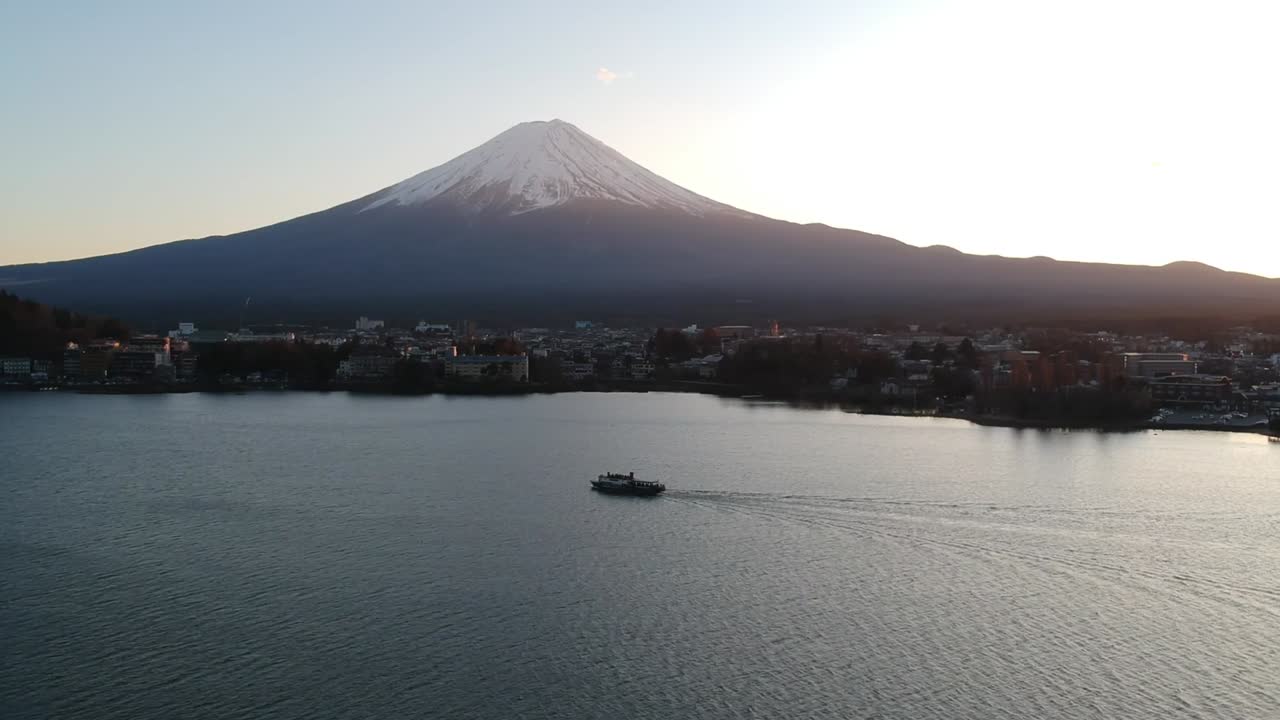 Scenic aerial view of Mount Fuji with a boat cruising across Lake Kawaguchi during sunset showing calm water, mountain reflection, and serene natural beauty with clear sky and horizon Outdoors