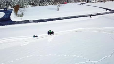 a panning - tracking, aerial, drone, birds eye view of a four wheeler quad driving in the winter snow