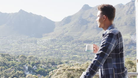 african american man drinking coffee on balcony with sunny mountain view, copy space, slow motion