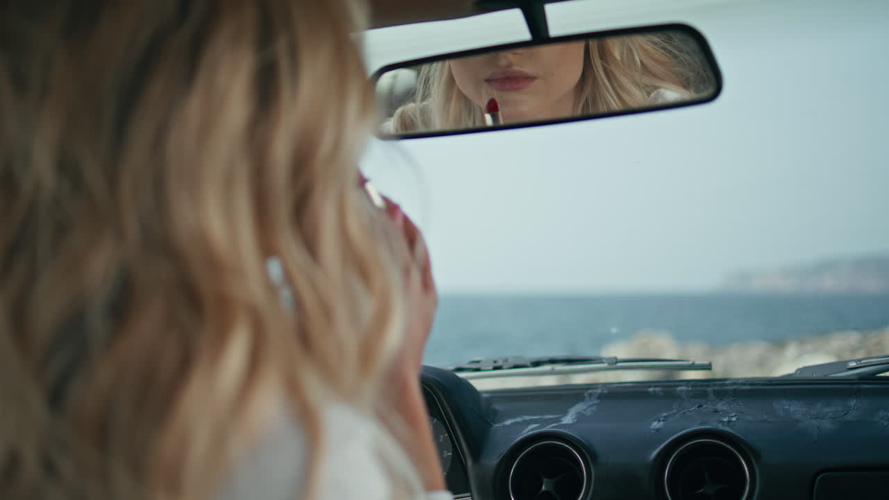 chica ajustando el espejo del coche sentada dentro del automóvil con lápiz labial rojo de primer plano