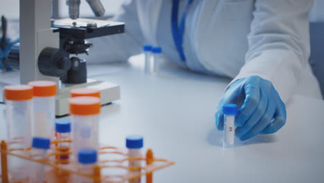 primer plano de un trabajador de laboratorio que lleva a cabo investigaciones utilizando un microscopio con un tubo de ensayo etiquetado pi