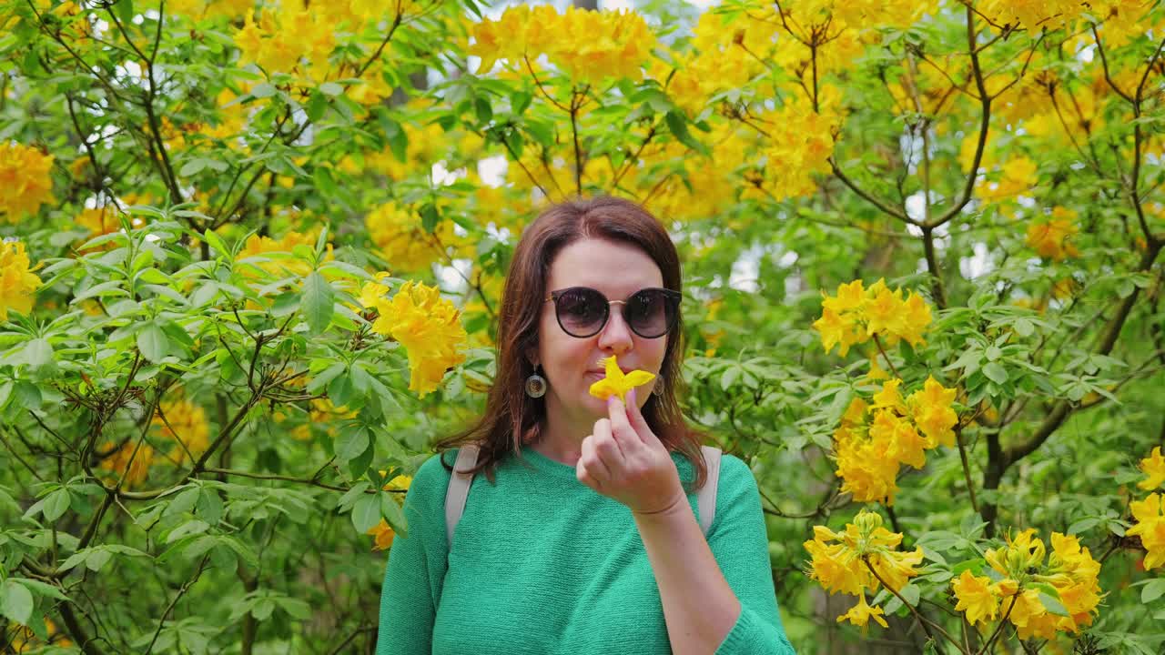 Foto de estilo de vida em close-up de mulher cheirando delicadamente uma vibrante flor de rododendro.