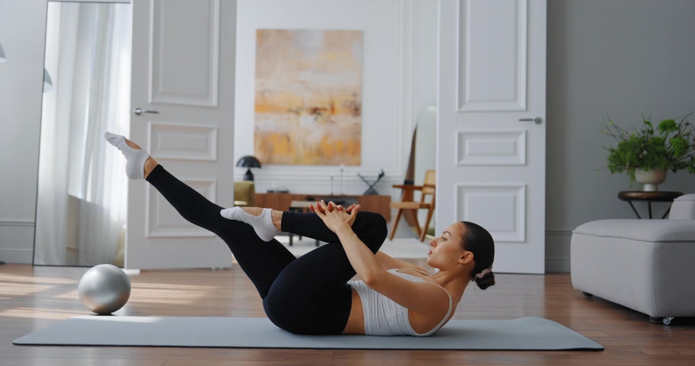 Giovane donna esegue l'esercizio single leg stretch sul tappetino a casa