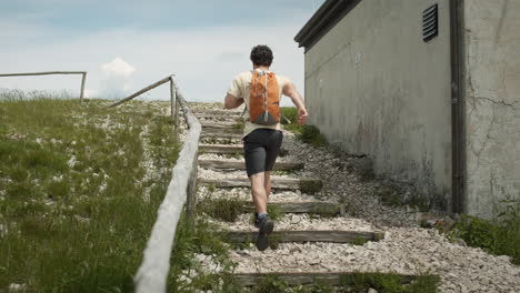 Hiker with an orange baackpack running up the stairs on path to the top of mountain Slavnik past the cottage