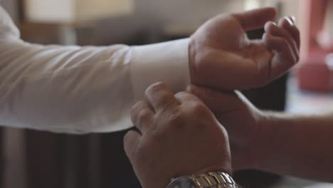 el novio recibe ayuda con los gemelos para la boda.