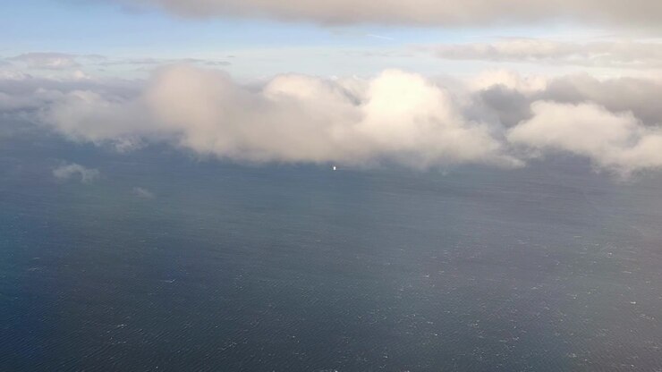 Skib sejler på et stort ocean under skyer. Set fra et flyvindue, der fremhæver rejse- og miljøtemaer.