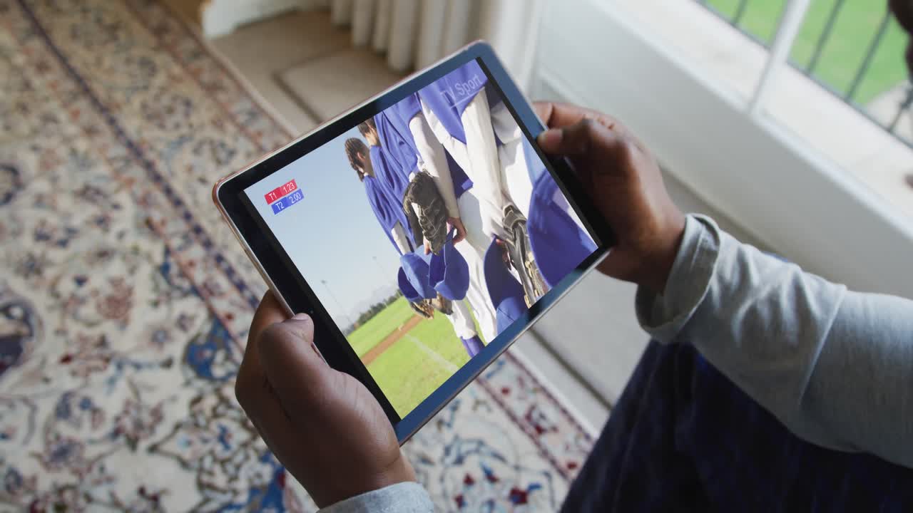 Composito di uomo seduto a casa che guarda una partita di baseball su tablet.