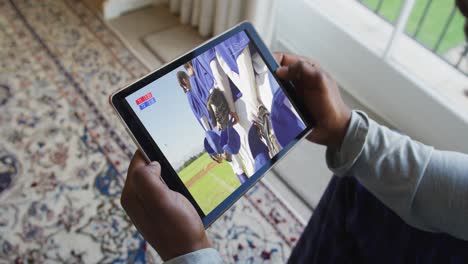 compuesto de un hombre sentado en casa viendo un juego de béisbol en una tableta