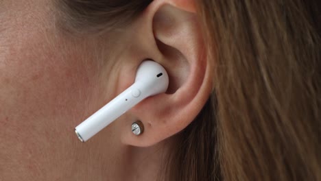 mujer de primer plano ponerse un auricular inalámbrico moderno blanco en el oído
