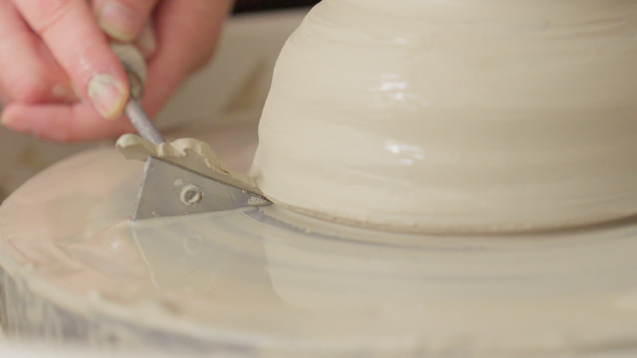 Skilled artisan masterfully completes a freshly made vase on a potter's wheel, using a tool to refine the bottom shape