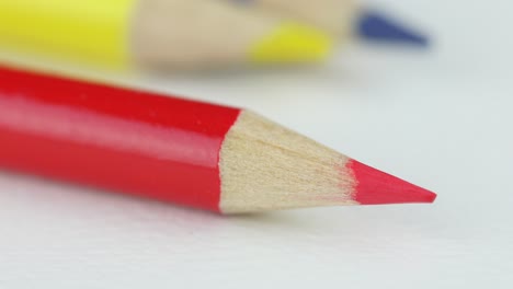 red sharpened pencil on white, yellow and blue in blurry background - close up