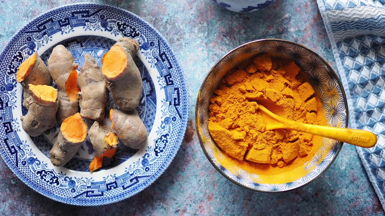 Radici di curcuma fresche e polvere in ciotole sul bancone della cucina
